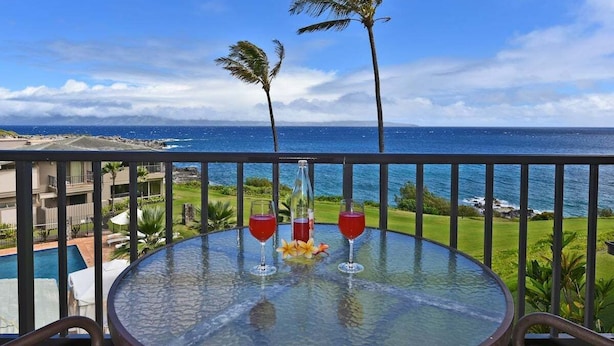 A balcony with a glass table, two red drinks, and a bottle, overlooking a pool and ocean view. - Upgraded 1BD OceanFront Villa w AC Pool - Kapalua Bay Villa 23B1 (Lahaina)