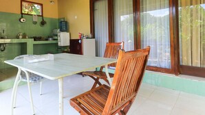 A dining area with a table and chairs, a kitchen area with a water dispenser, and a window with curtains. - Sunari Guest House (Canggu)