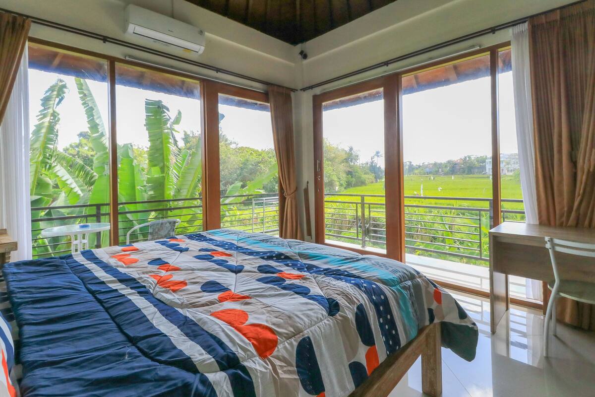 A room with a bed, a desk, and large windows with curtains.