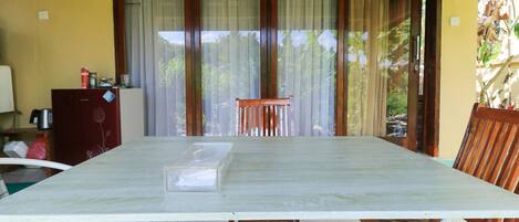 A dining area with a table, chairs, and a view through large windows.