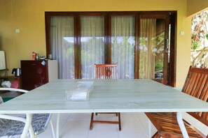 A dining area with a table, chairs, and a view through large windows. - Sunari Guest House (Canggu)