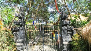 A stone gate with a metal fence, surrounded by lush greenery and trees. - Sunari Guest House (Canggu)