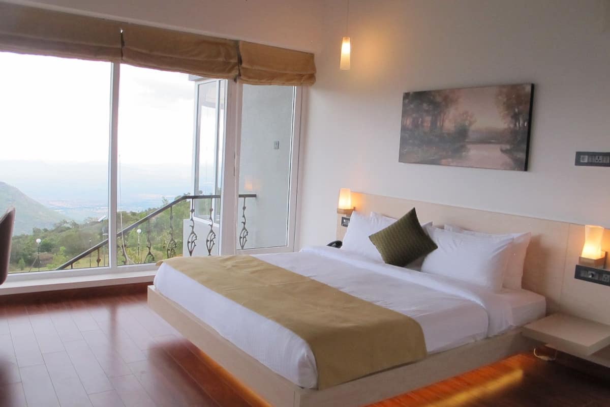 A hotel room with a large bed, a view of the outdoors, and a painting on the wall.