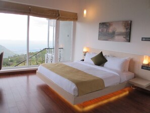 A hotel room with a large bed, a view of the outdoors, and a painting on the wall.