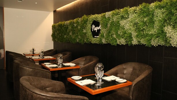 Un restaurant avec des fauteuils en cuir marron foncé, des tables en bois et un mur vert orné d’une enseigne indiquant « Naples ».