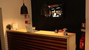 Un comptoir d’accueil avec un ordinateur portable, une plante en pot et un téléviseur diffusant une scène animée.
