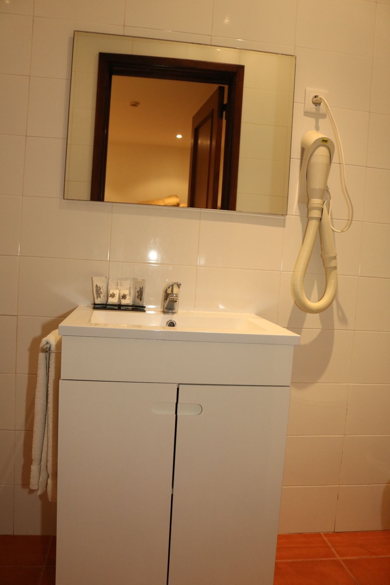A bathroom with a white sink, a mirror above it, and a hairdryer on the wall.