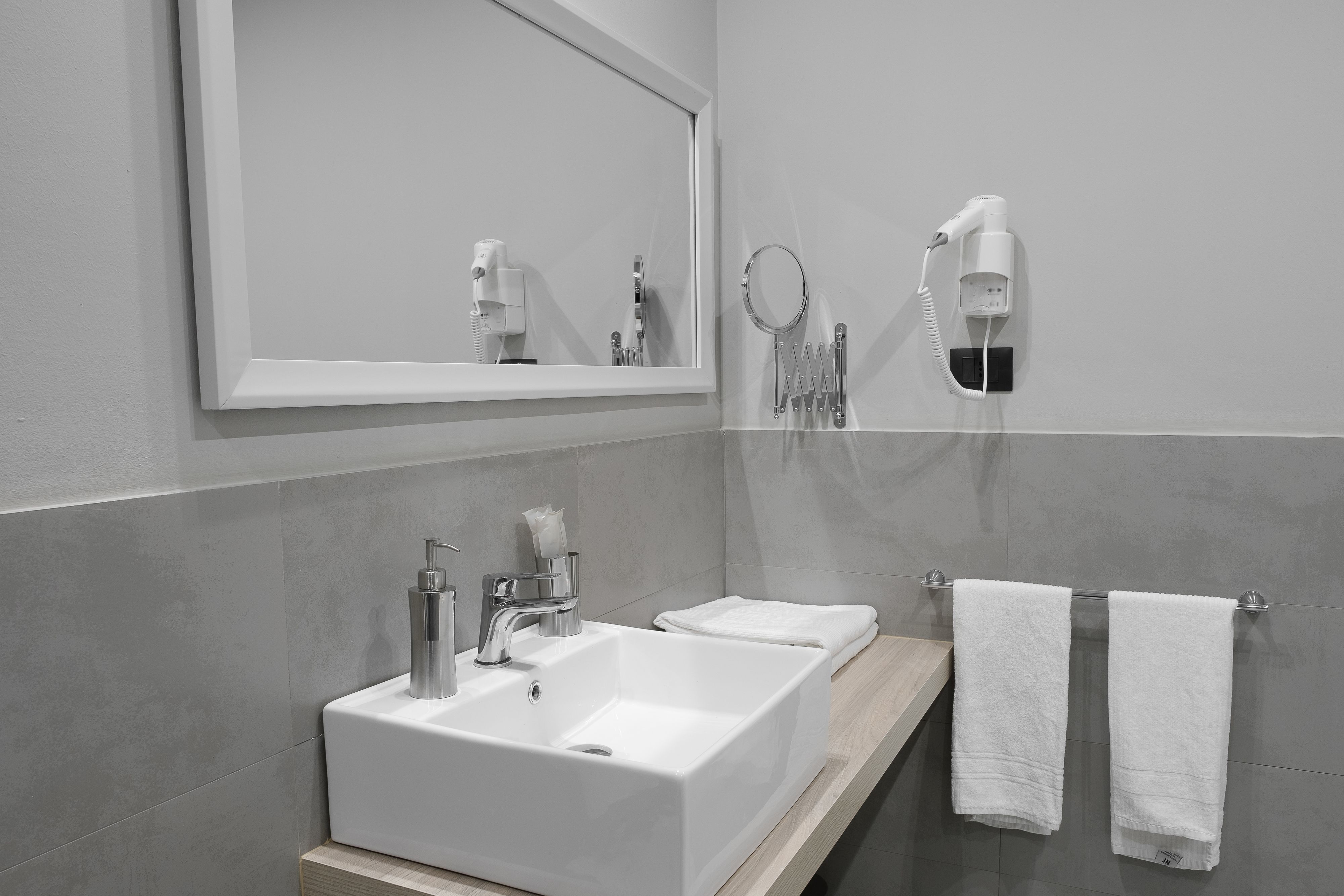 A modern bathroom with a large mirror, two sinks, and a hairdryer mounted on the wall.