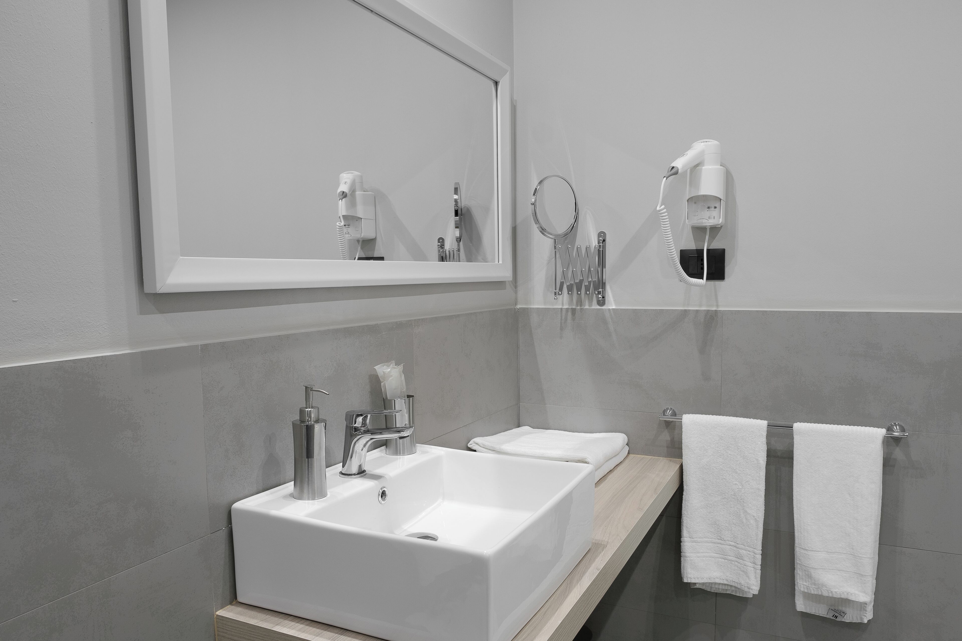 A modern bathroom with a large mirror, two sinks, and a hairdryer mounted on the wall.