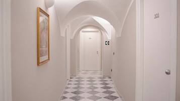 A hallway with a checkered floor, white walls, and a framed picture on the left.