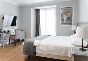 A hotel room with a bed, a desk, a chair, a television, and a window with curtains.