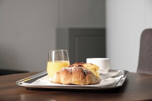 A breakfast tray with a pastry and a glass of orange juice on a wooden table.