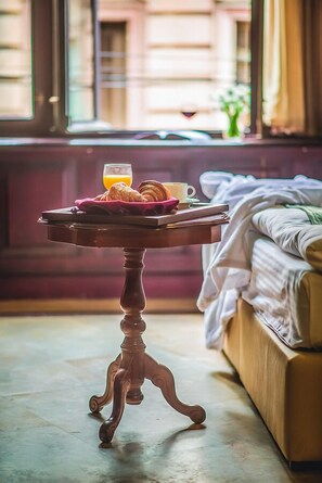 A breakfast tray with croissants, a cup, and orange juice on a wooden table in a room with a bed and a window. - Emigrant (Tbilisi)