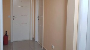 Un pasillo con dos puertas blancas, un extintor rojo y un interruptor de luz en la pared.