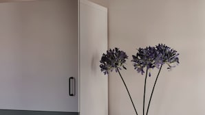 Et hvidt skab med sort håndtag, en grå nedre del og en hvid vase med lilla blomster på en væg.