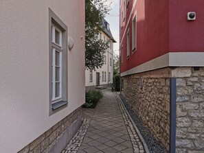 Un estrecho callejón entre edificios, con una pared de piedra a un lado y un edificio rojo al otro.