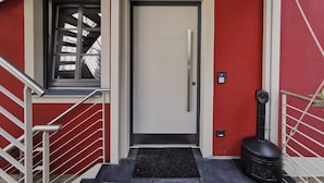 En rød og hvid bygning med facade, dør, vindue og en sort skraldespand.