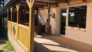 En overdækket terrasse med betongulv, træbjælker og en murstenssøjle.