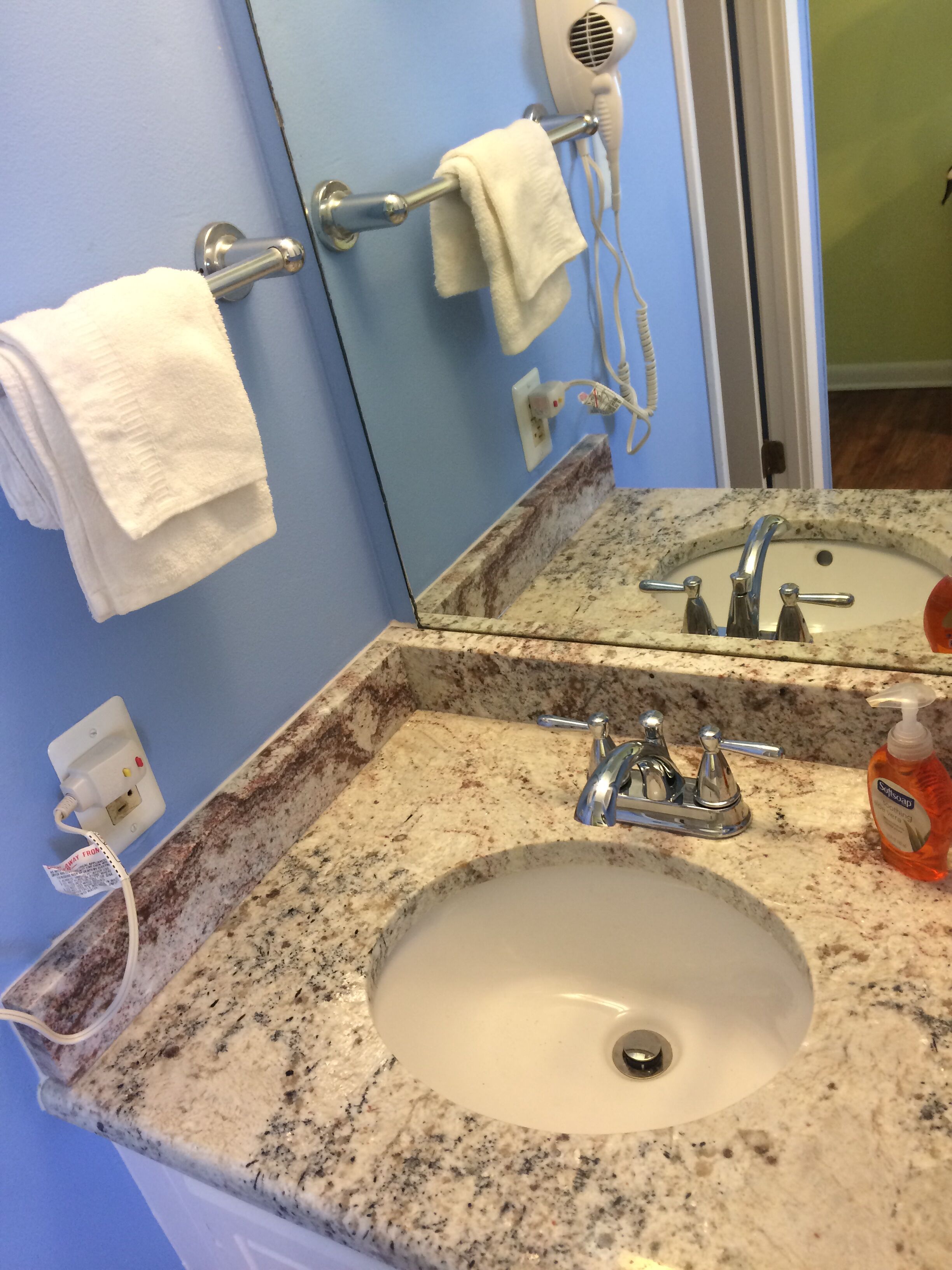 A bathroom with a granite sink, a mirror, a hairdryer, and a towel rack.