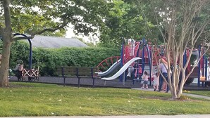 A playground with slides and climbing structures, surrounded by trees and benches.