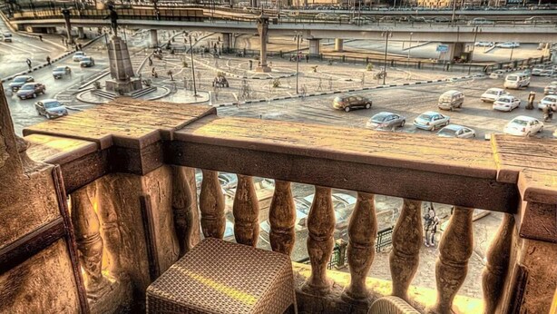 A balcony with wicker furniture overlooking a busy urban street with buildings and a bridge. - Tahrir Plaza Suites (Cairo)