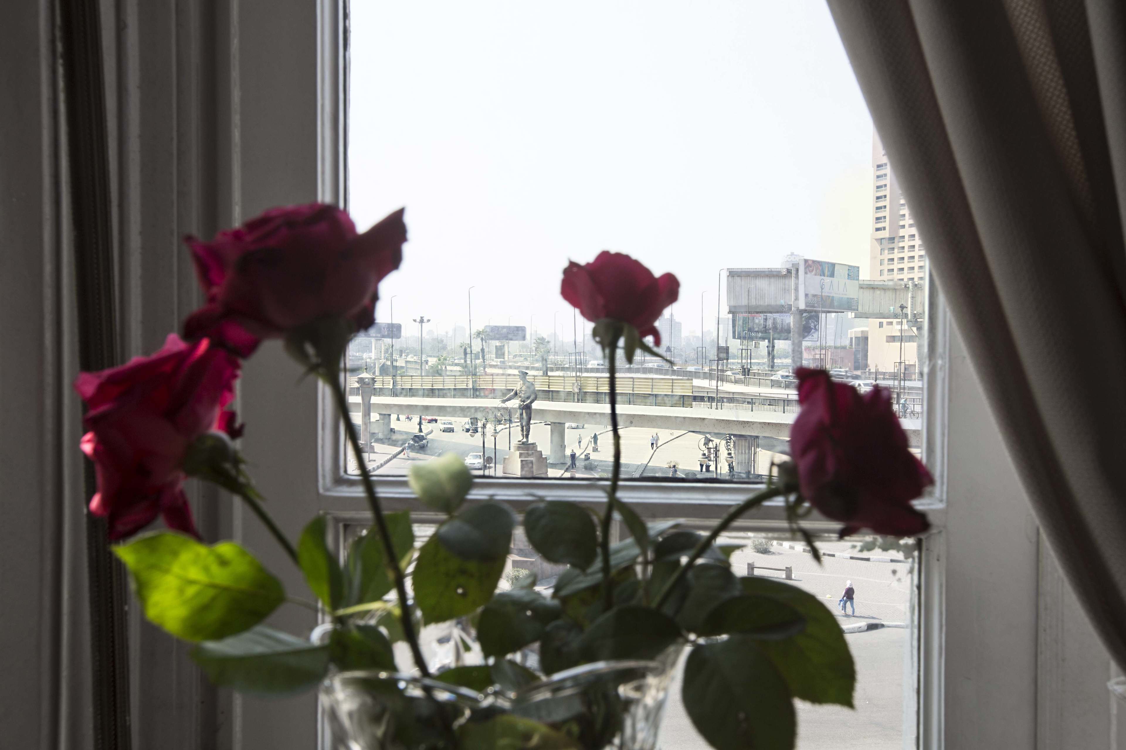 Uma janela com vista para a paisagem urbana e um vaso com rosas.