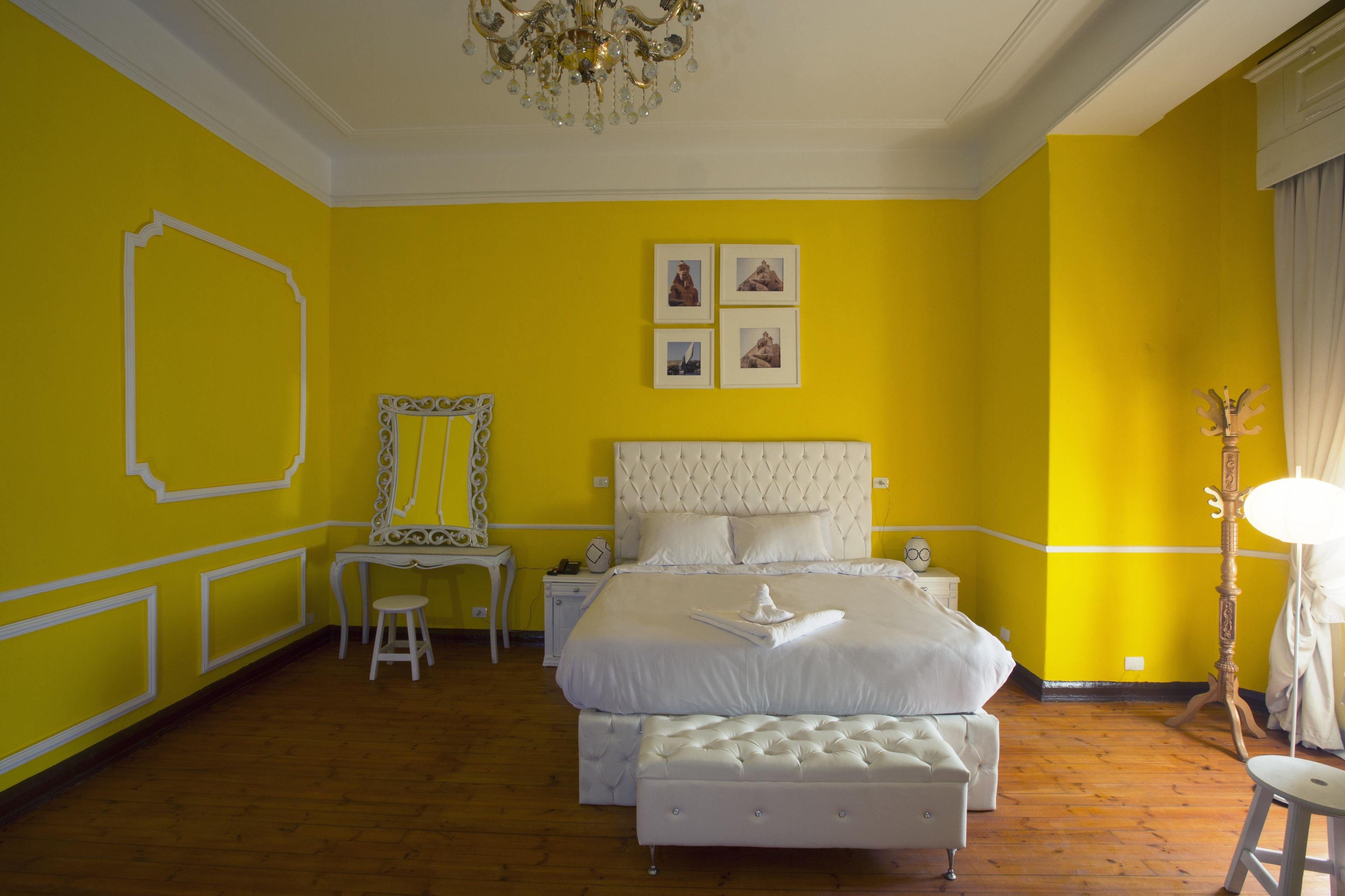 A bright yellow bedroom with a large bed, a nightstand, a chair, and a mirror.
