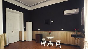 A room with a wooden floor, a white door, a white sofa, a small white table with two stools, and a wall-mounted air conditioner. - Tahrir Plaza Suites (Cairo)