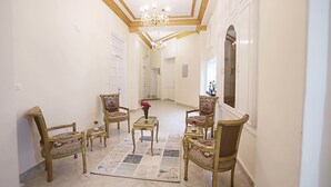 A spacious hallway with ornate chairs and a chandelier, leading to a door. - Tahrir Plaza Suites (Cairo)