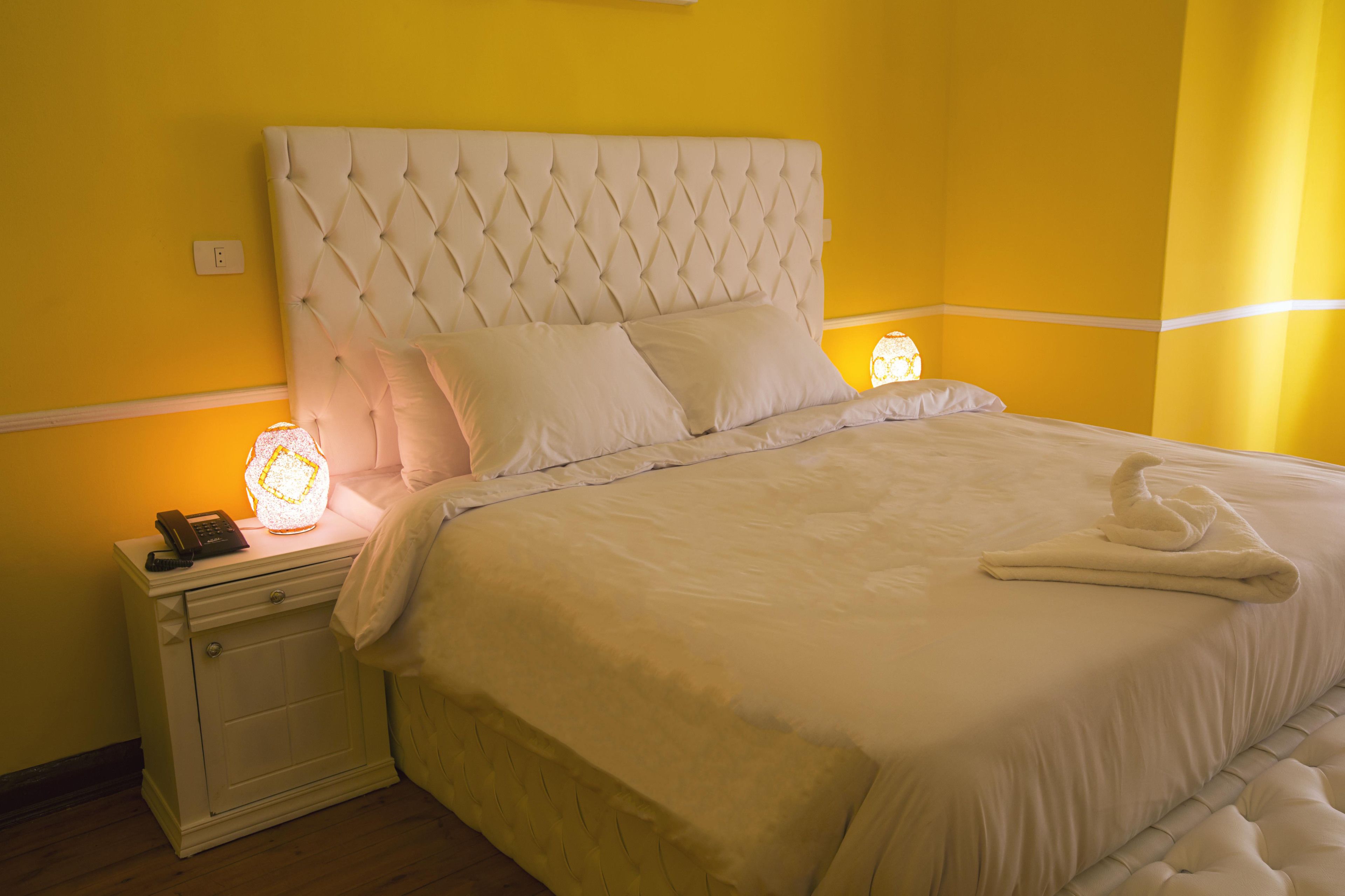 Una cama con cabecera capitonada, ropa de cama blanca y una lámpara de noche.