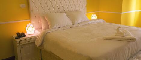 Una cama con cabecera capitonada, ropa de cama blanca y una lámpara de noche.