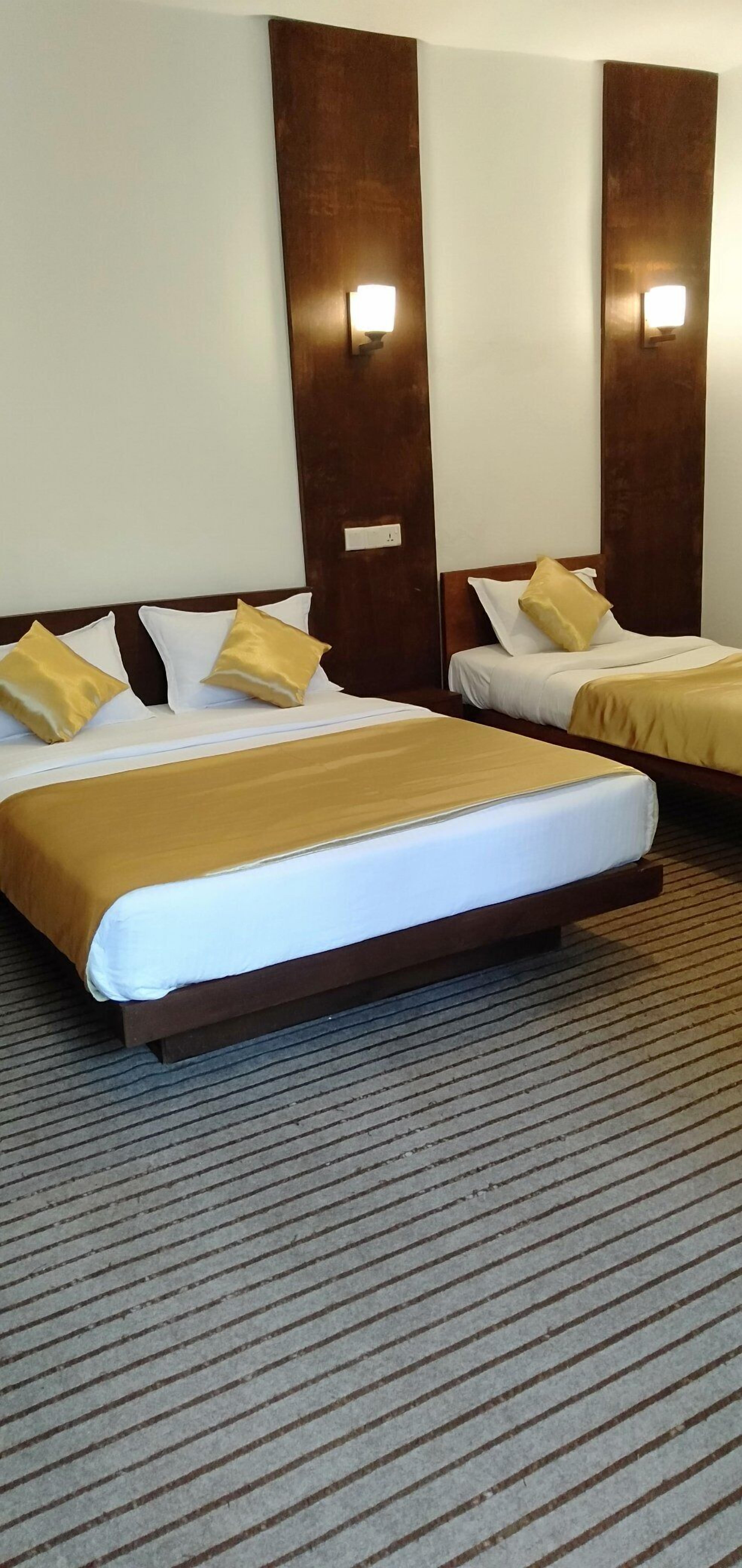 Ein Hotelzimmer mit zwei Betten, jeweils mit einem hölzernen Kopfteil, weißer Bettwäsche und einer braunen Decke.