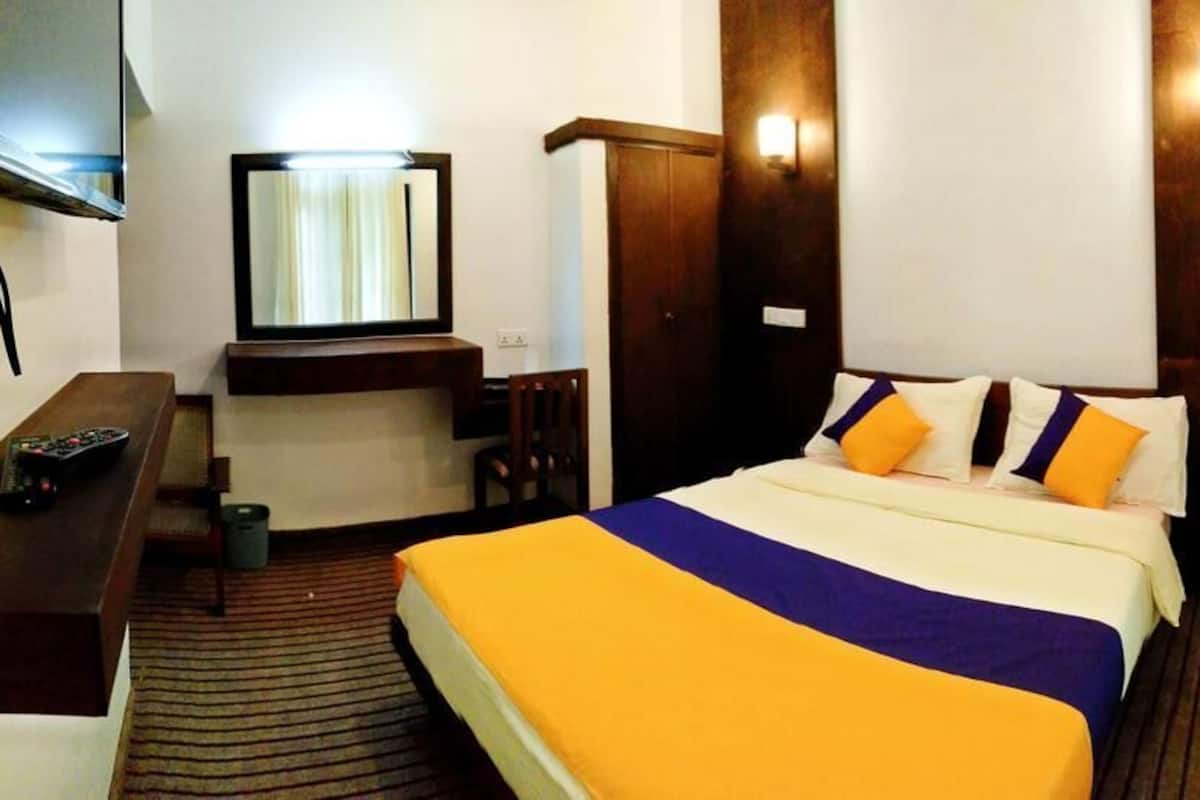 A hotel room with a bed, a desk with a chair, a TV, and a mirror.