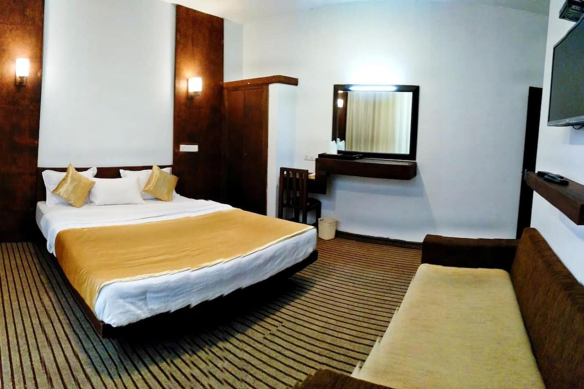 A hotel room with a large bed, a bedside table, a TV, and a bench.