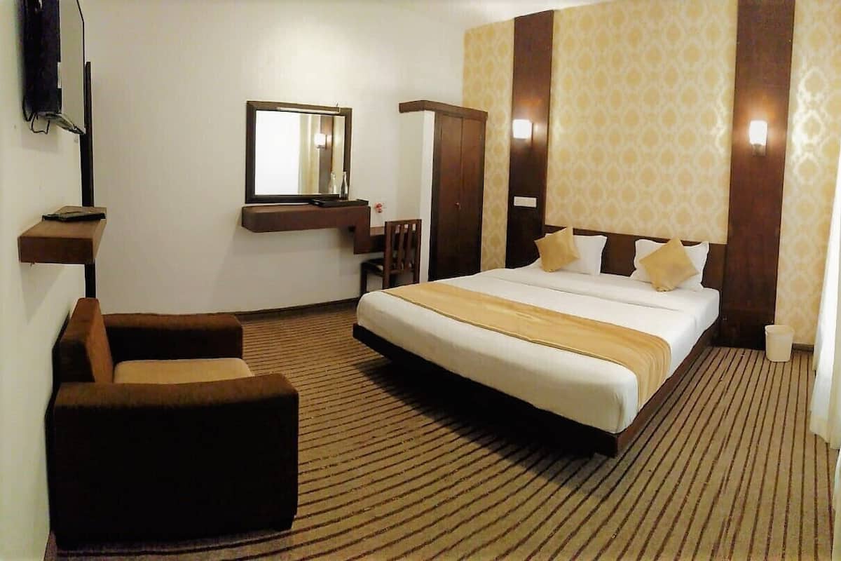 A hotel room with a large bed, a desk with a chair, a mirror, and a wardrobe.