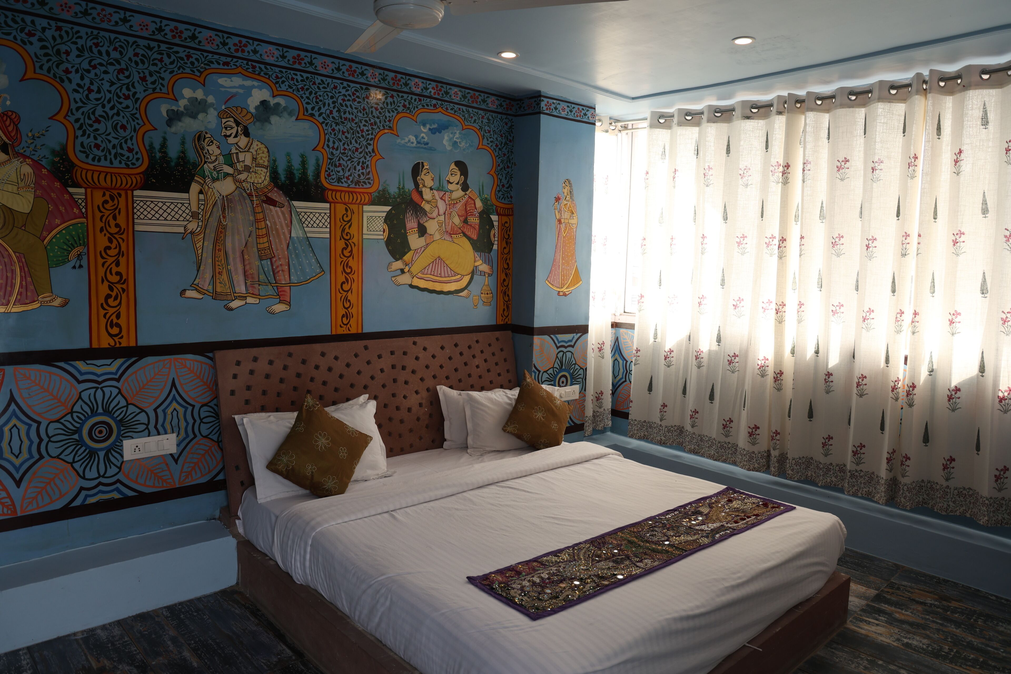 Un dormitorio con una cama grande, decoración en la pared y un ventanal con cortinas.