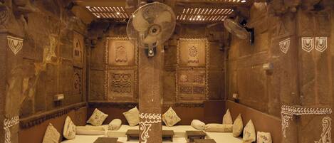 A room with stone walls, a central pillar, and multiple seating areas with cushions.