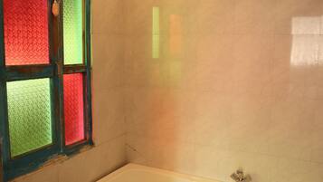 A bathroom with a bathtub, a window with colored glass panes, and a wooden floor.