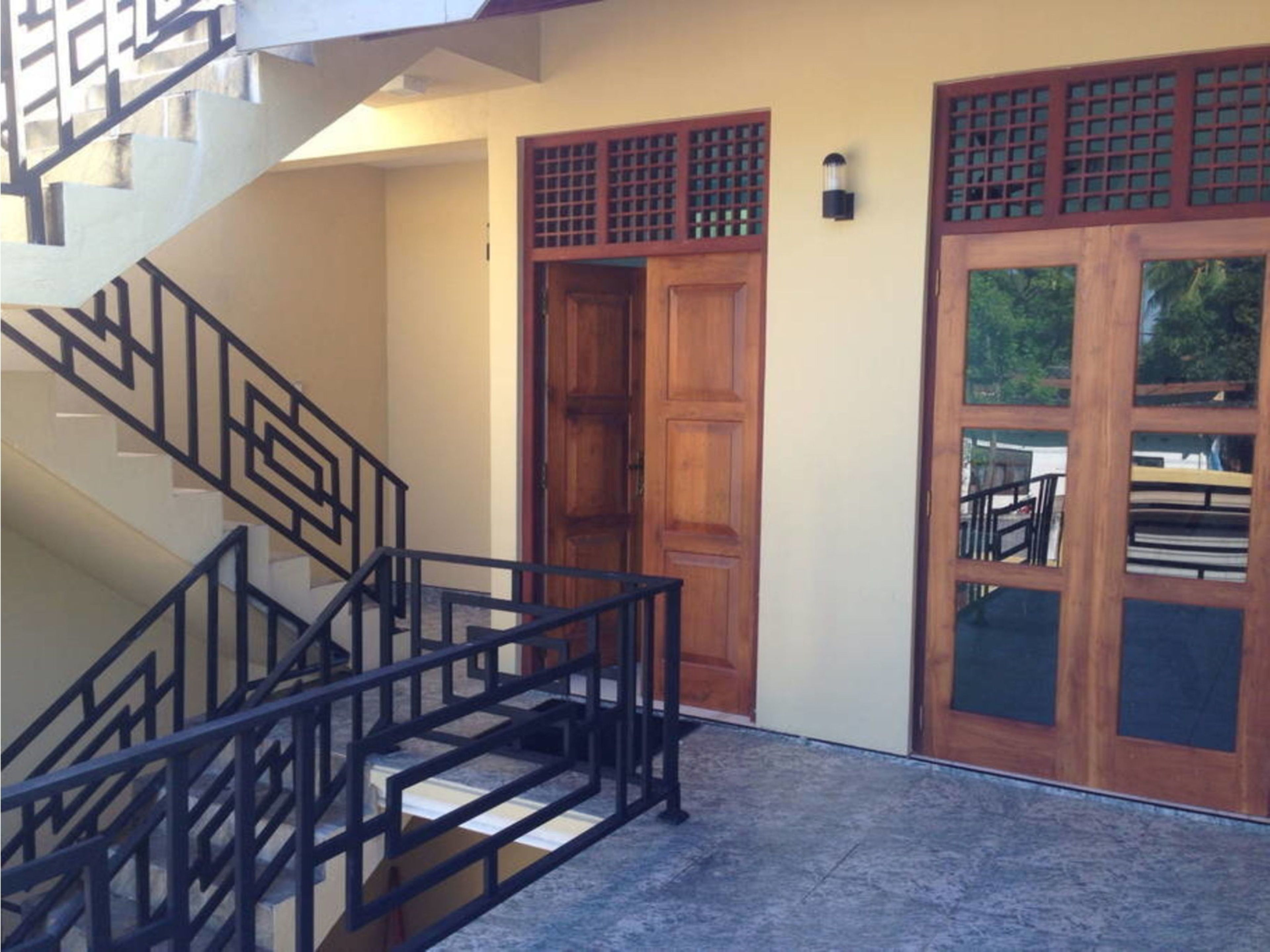A staircase with a geometric railing, a wooden door with glass panels, and a wall-mounted light fixture.