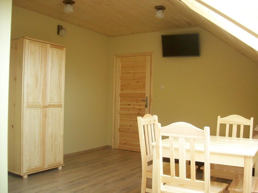 A room with a wooden wardrobe, a wooden door, a table with chairs, and a television mounted on the wall.