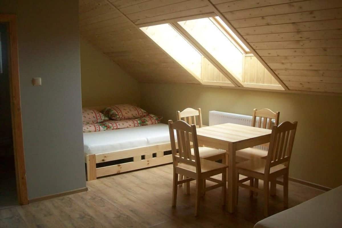 Un dormitorio tipo buhardilla pequeño con techo inclinado, tragaluz, cama, mesa y sillas.
