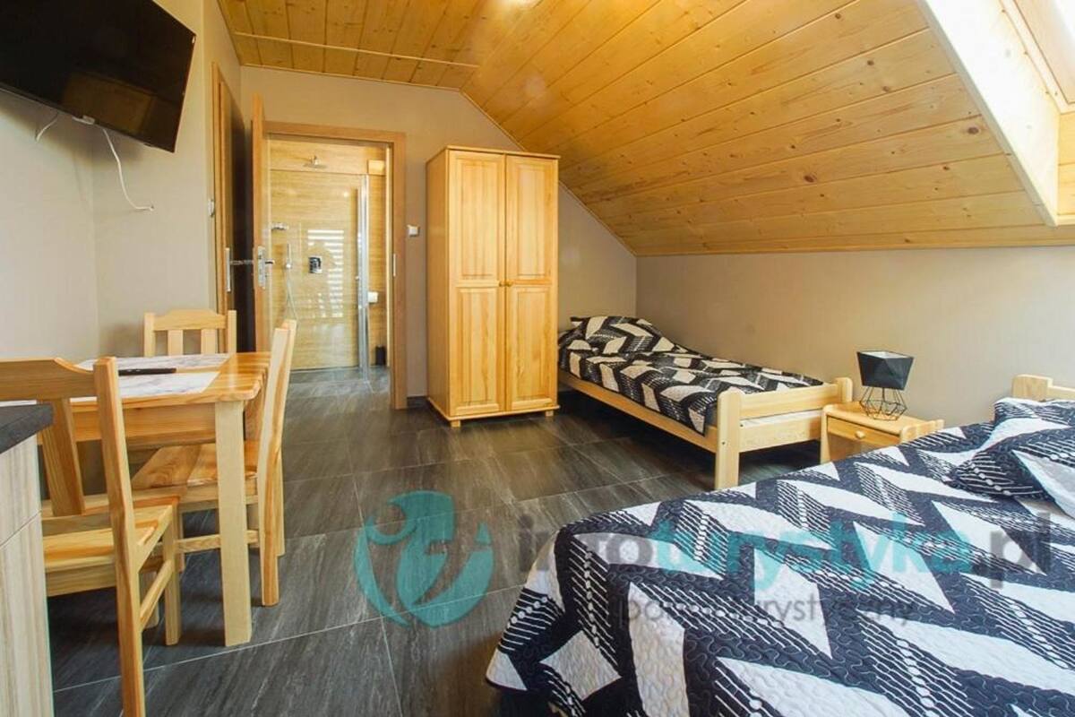Una habitación con techo de madera, cama con ropa de cama estampada, escritorio con sillas y armario.