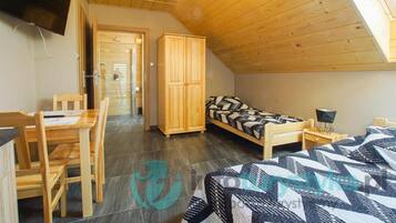 A room with a wooden ceiling, a bed with patterned bedding, a desk with chairs, and a wardrobe.