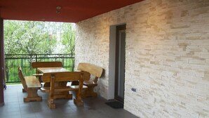 Un porche techado con mesa y bancos de madera, paredes de piedra y vista a la vegetación.