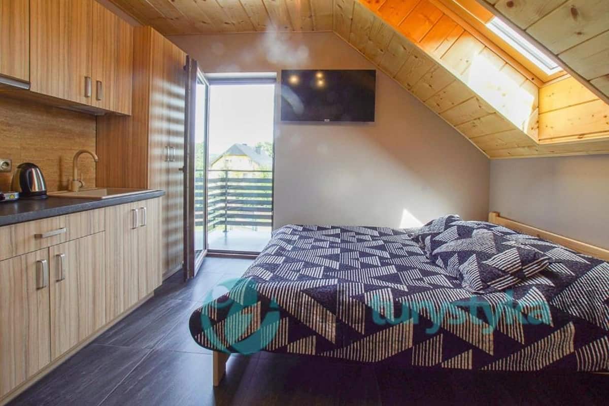 Un dormitorio compacto con una cama, un televisor montado en la pared y un tragaluz.