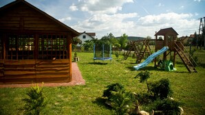 Una cabaña de madera con un sendero de ladrillo que la conduce, rodeada de un área cubierta de césped con juegos infantiles.
