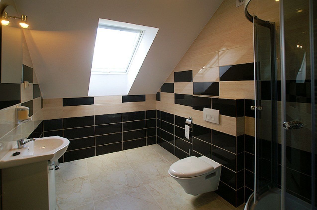 Um banheiro moderno com claraboia, paredes com azulejos preto e branco, uma pia branca e box de vidro para o chuveiro.