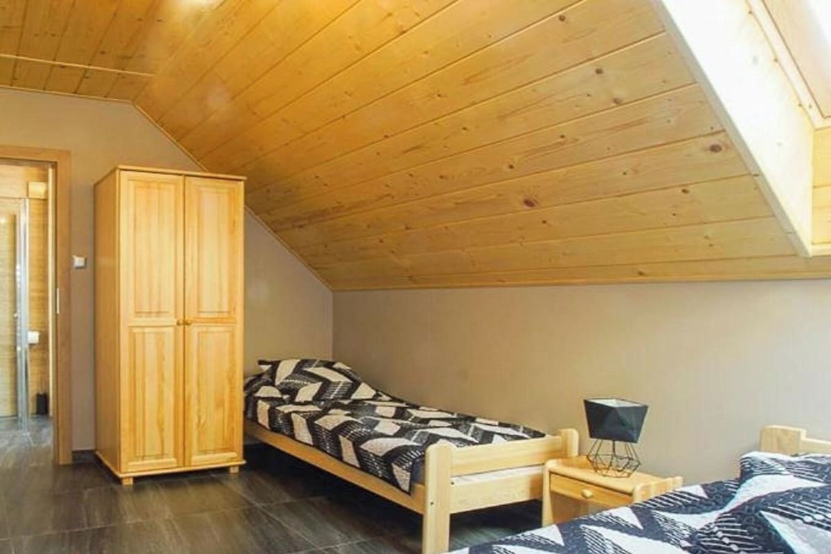 Quarto pequeno com cama, guarda-roupa de madeira, escrivaninha e cadeira.
