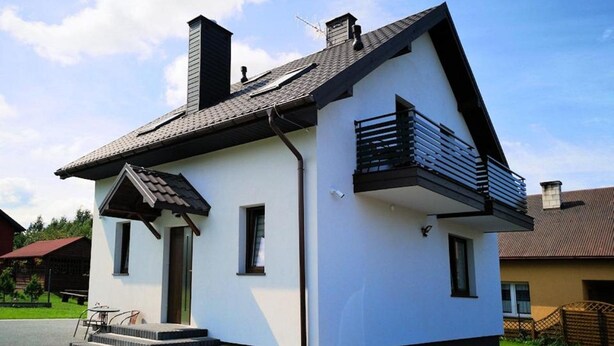 Una casa moderna de dos pisos con techo pronunciado, un pequeño porche delantero y un balcón en el nivel superior.