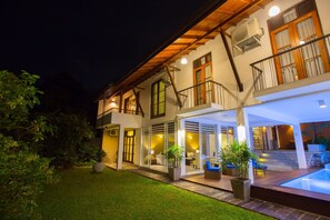Ein zweistöckiges Haus mit Balkon, Pool und einer gut beleuchteten Außenanlage.
